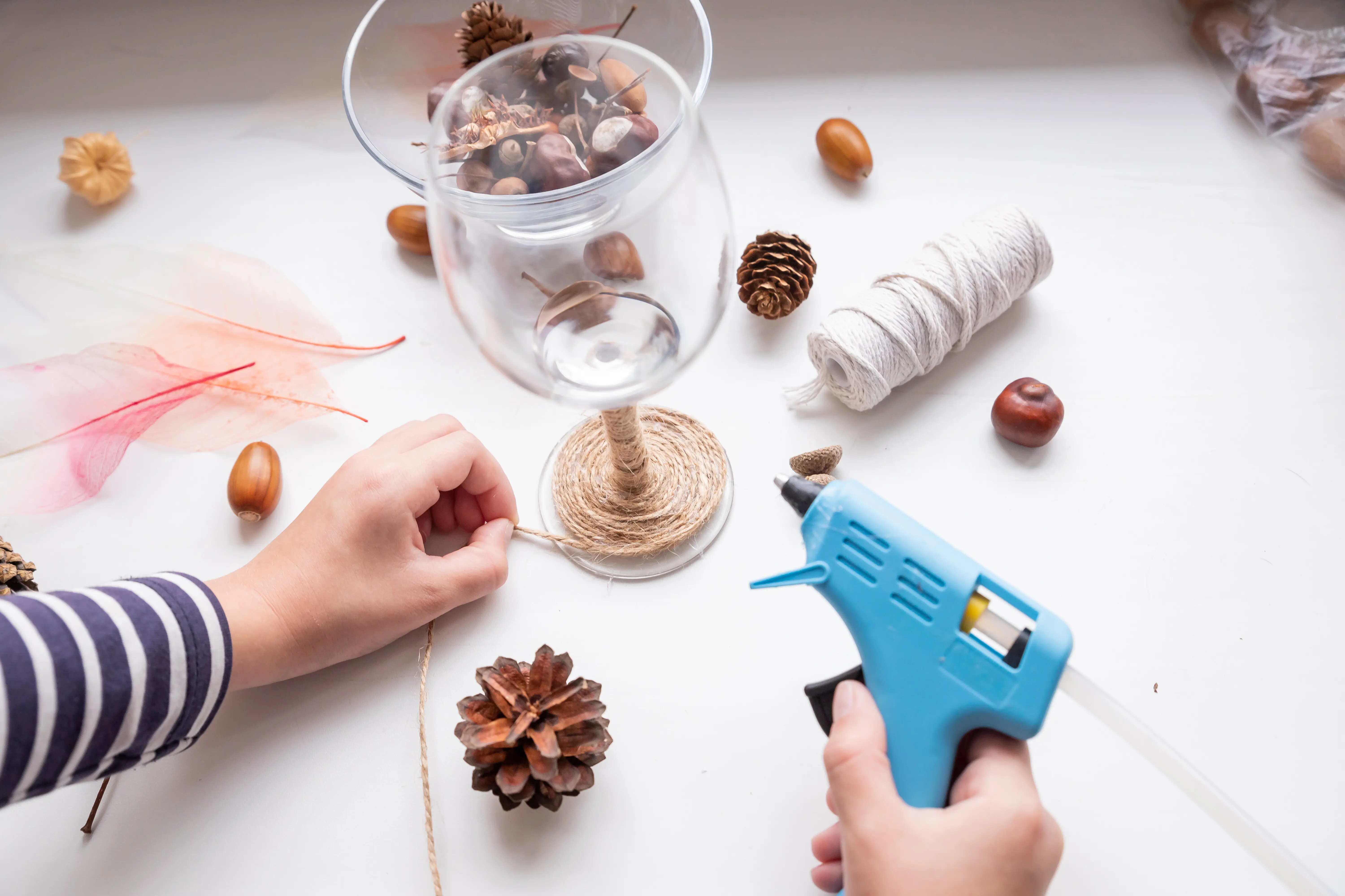 Schritt-für-Schritt-DIY-Anleitung für eine Herbstkomposition im Glas als DIY-Bastelarbeit. Geschenk von Kindern, Set für Kreativität. Schritt 2: Ein Kind klebt Fäden auf ein Glas.