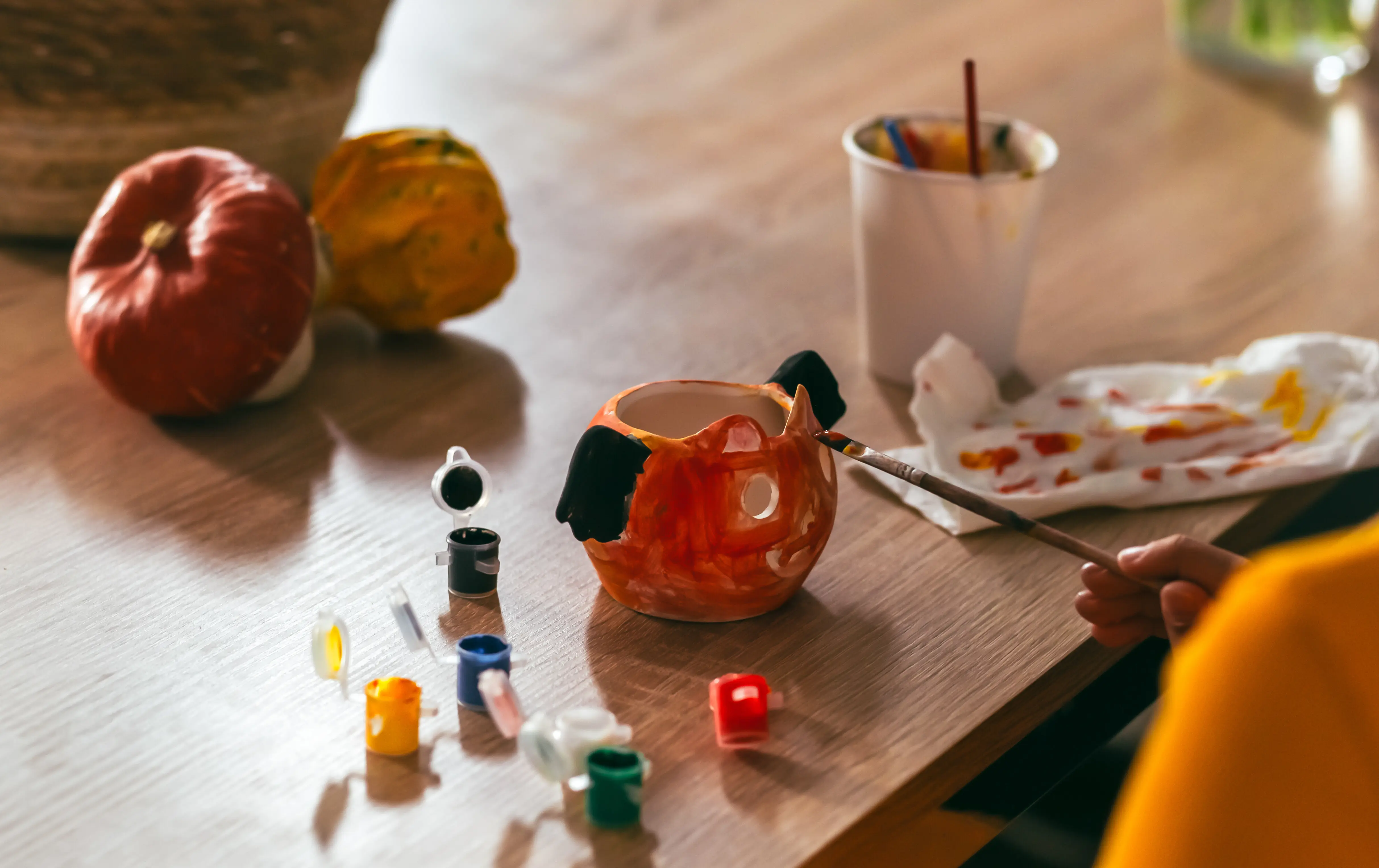 Ein kleines Mädchen bemalt einen handgemachten Kürbis aus Ton – Halloween-Party, Basteln für Kinder.