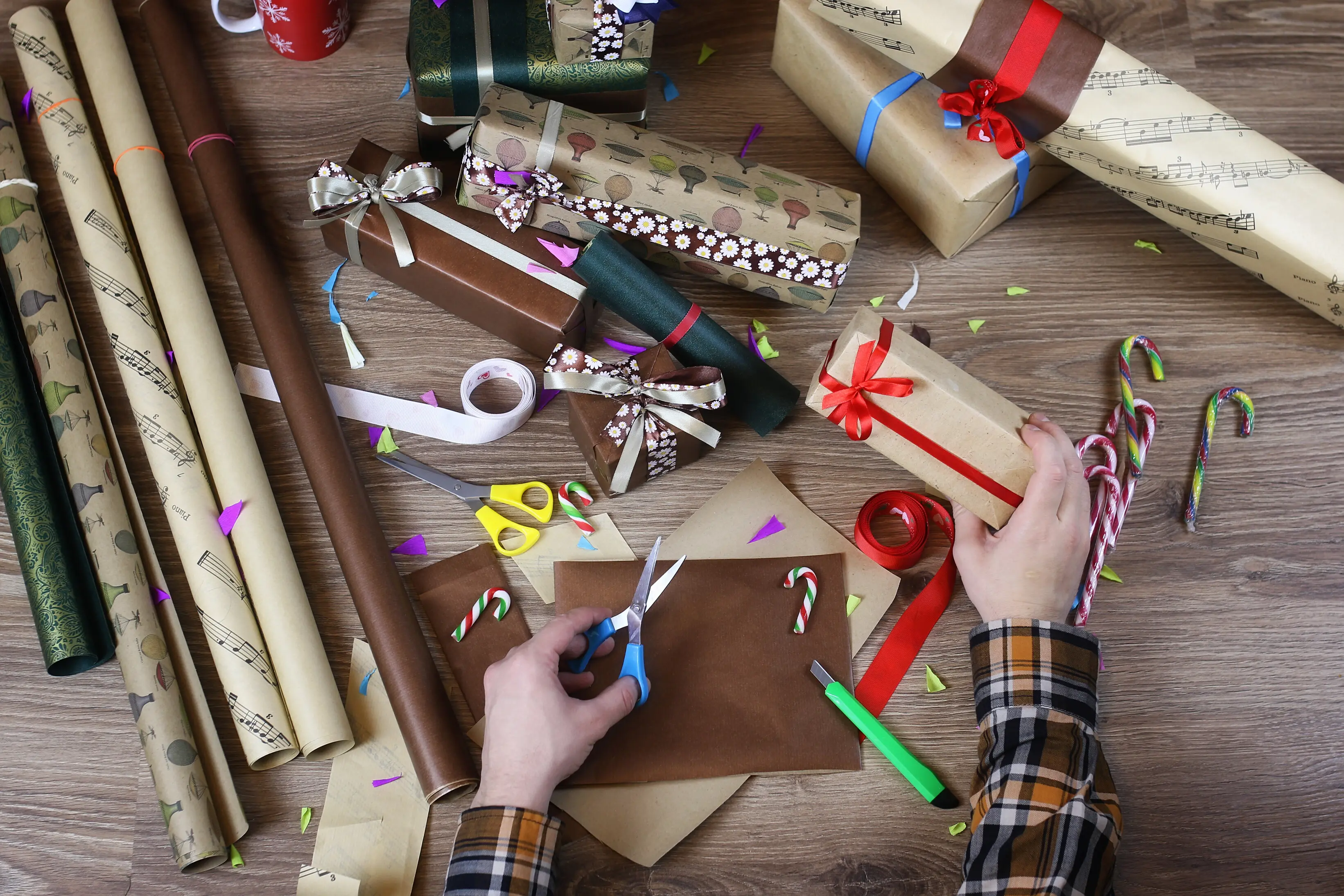 Hand beim Einpacken mit Geschenkpapier für den Feiertag Weihnachten, mit Geschenkband und Schleifen.