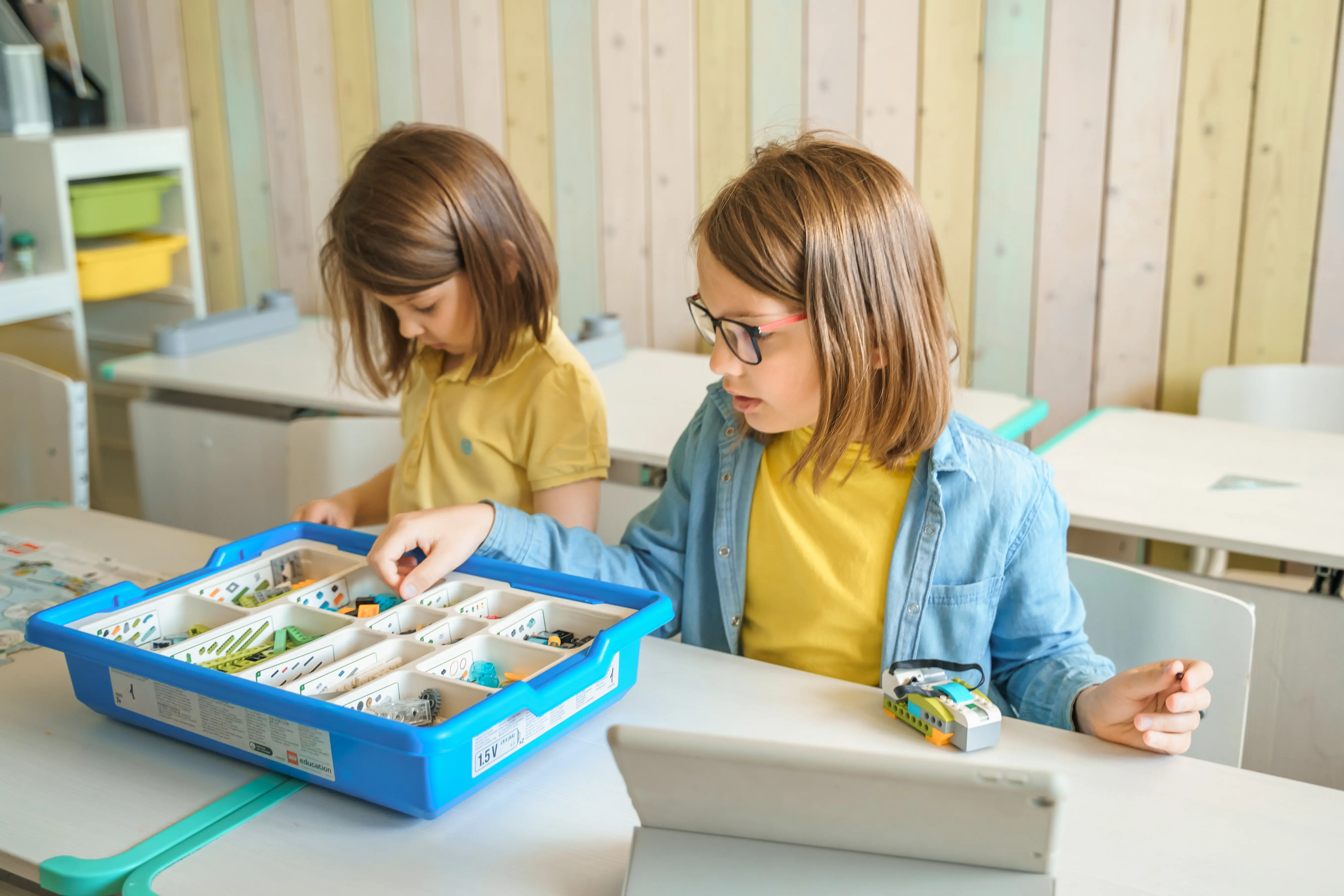 Programmierungsarbeit und Robotiklernen in der Grundschule: Kinder/Schüler bauen einen Roboter aus Baukastenteilen nach Anleitungen auf dem Tablet zusammen, starten ihn und programmieren ihn; MINT-Bildung im naturwissenschaftlich-technischen Unterricht.
